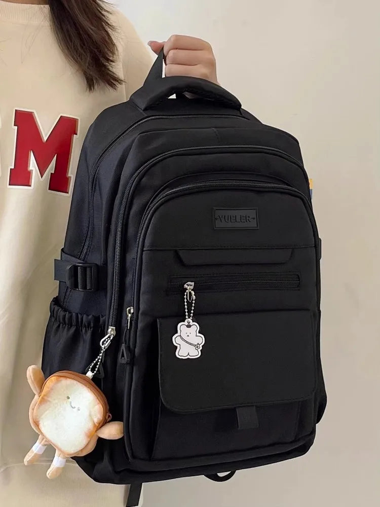 Sac à dos noir avec plusieurs poches et un accessoire mignon, idéal pour le lycée et le transport d'ordinateur.