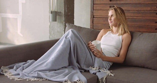 Femme détendue sous une couverture avec une tasse sur son canapé