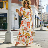 Femme souriante en robe longue fleurie orange et jaune, manches à volants, posant en plein jour
