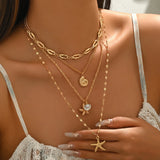 Femme portant le collier multi-rangs doré avec pendentifs marins, main posée sur le décolleté