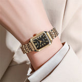 Montre carrée dorée avec cadran noir portée au poignet d'une femme, finition chic et contrastée.