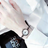 Montre bracelet noire avec cadran blanc à chiffres arabes portée par une femme