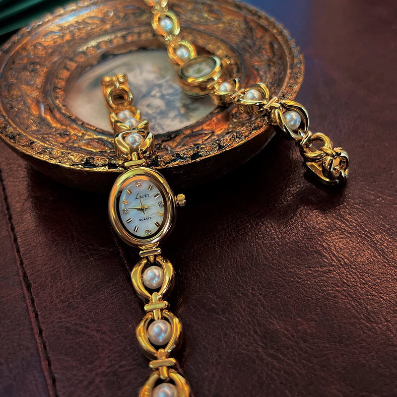 Montre ovale dorée pour femme avec bracelet orné de perles, posée sur un plateau vintage