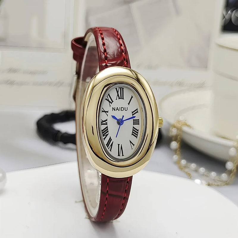 Montre ovale vintage avec bracelet en cuir bordeaux et cadran doré, posée sur un support