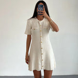Robe courte tricotée blanche femme avec boutons métal, style épuré pour un look sophistiqué cet automne.