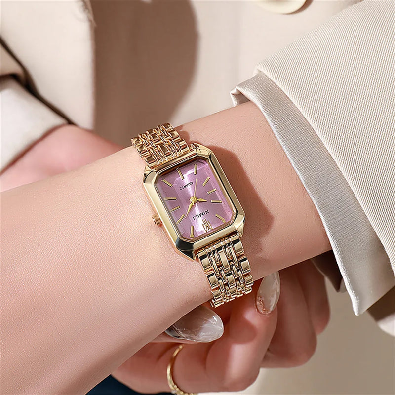 Montre carrée dorée avec cadran rose lavande portée au poignet d'une femme, style élégant.