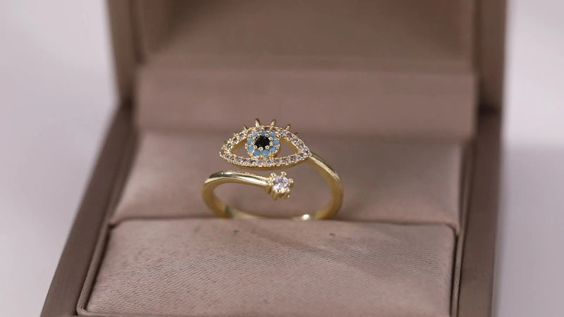 Bague ajustable œil protecteur doré avec zircons bleus et blancs sur fond beige