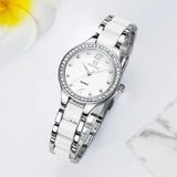 Montre quartz femme raffinée bracelet bicolore blanc et argenté, cadran blanc index romains et strass, posée sur une surface blanche