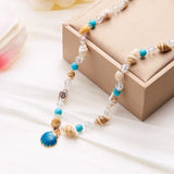 Collier coquillages cauris et perles dorées, porté avec un haut blanc
