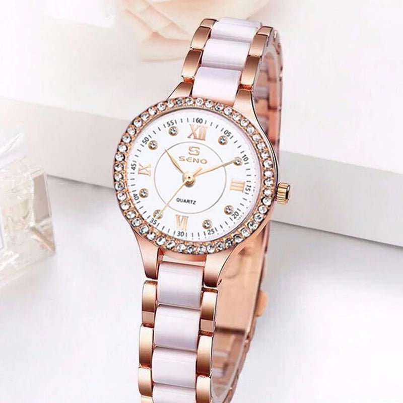 Montre quartz femme élégante bracelet bicolore blanc et doré rose, cadran blanc index romains et strass, posée sur une surface blanche
