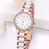 Montre quartz femme élégante bracelet bicolore blanc et doré rose, cadran blanc index romains et strass, posée sur une surface blanche