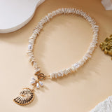 Collier ras du cou avec petites pierres blanches et coquillage doré sur fond beige