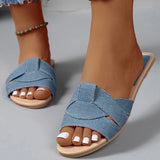 Pieds de femme portant des sandales plates tressées bleu ciel en jean sur un sol gris