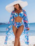 Femme en maillot de bain 3 pièces imprimé bleu vif et floral sur la plage, regardant l'océan