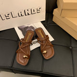 Sandales plates marron pour femme avec lanières et boucle dorée, posées sur un support en cuir noir