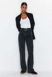 Femme portant un jean vintage taille haute évasé en denim noir avec un top blanc et blazer noir.