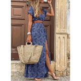 Femme portant une robe longue bleu marine à motifs paisley, fendue sur le côté, avec ceinture marron et sac en paille