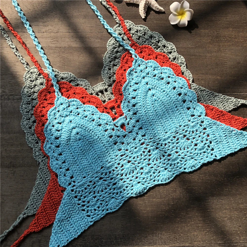 Bralettes crochet bohèmes de différentes couleurs (bleu ciel, corail, gris) empilées sur fond bois, avec étoile de mer et fleur de frangipanier