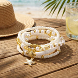 Composition de bracelets bohèmes blancs et dorés avec perles et breloques étoiles de mer, sur fond de plage
