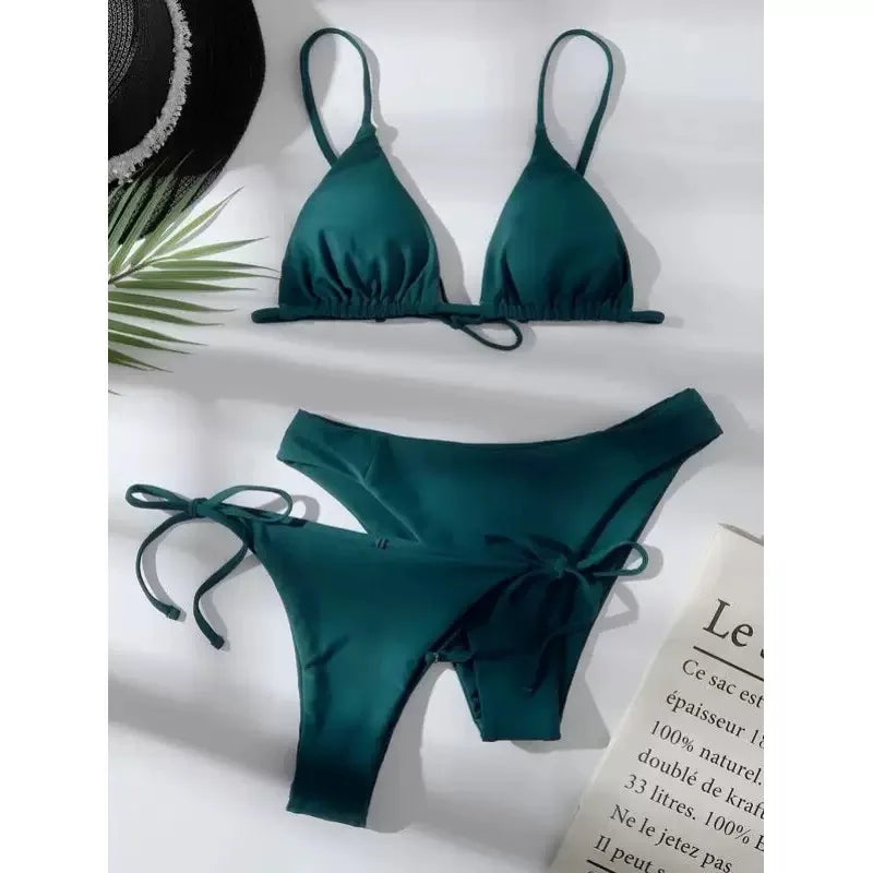 Bikini push up vert émeraude 3 pièces, haut triangle et deux bas, un taille basse et un à nouer, posé sur une surface claire avec feuillage et chapeau