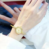 Montre bracelet rose doré avec cadran blanc à chiffres romains portée au poignet
