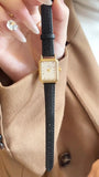 Montre femme vintage carrée GEDI, bracelet cuir noir, boîtier doré, tenue par une main aux ongles longs