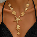 Collier doré avec pendentifs coquillages variés et une grande étoile de mer centrale, porté sur un décolleté noir