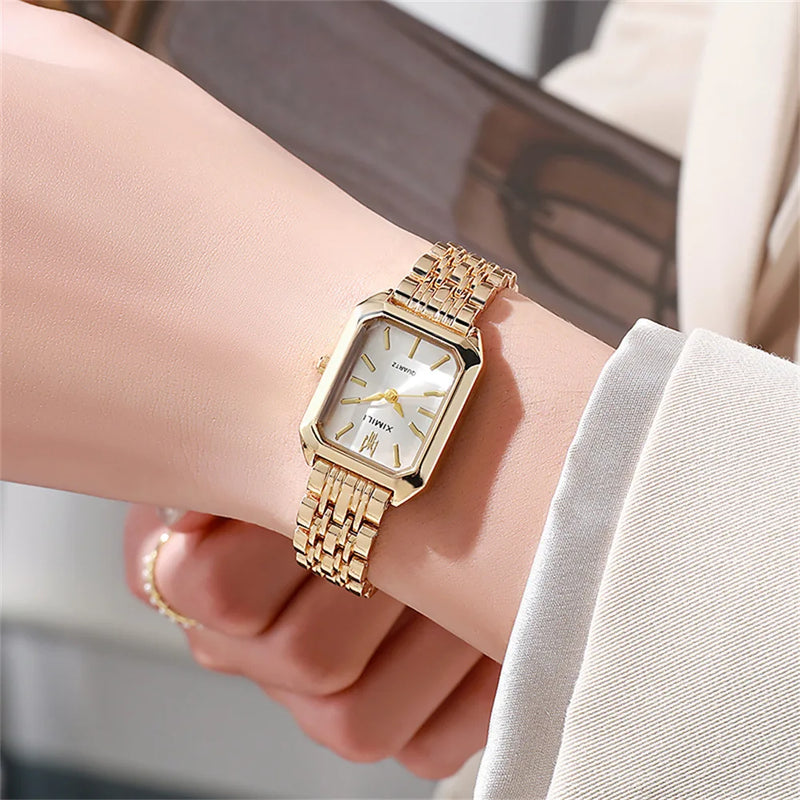 Montre femme carrée dorée avec cadran blanc portée sur un poignet féminin, assortie à une bague dorée