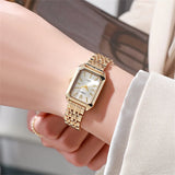 Montre carrée dorée avec cadran blanc portée au poignet d'une femme, détail du bracelet en maille.