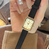 Montre femme vintage carrée GEDI, bracelet cuir noir, boîtier doré, tenue par une main