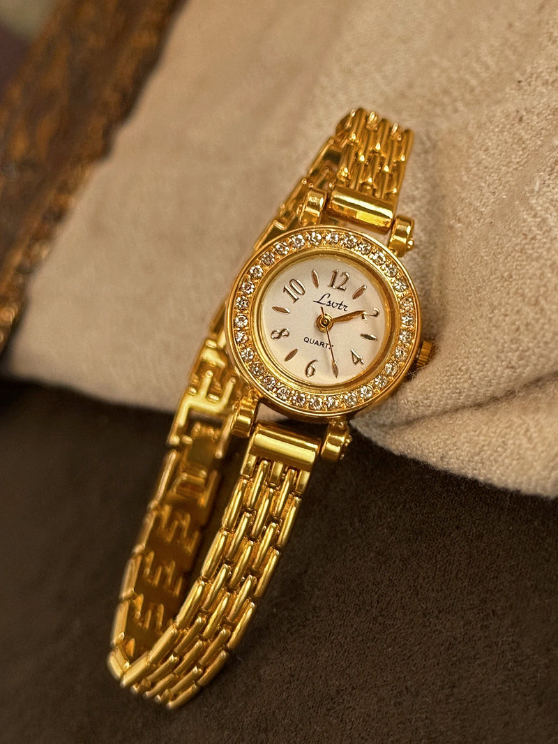 Gros plan d'une montre quartz dorée pour femme avec cadran nacre, strass et chiffres arabes