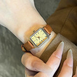 Montre femme vintage carrée GEDI, bracelet cuir marron, boîtier argenté, tenue par une main