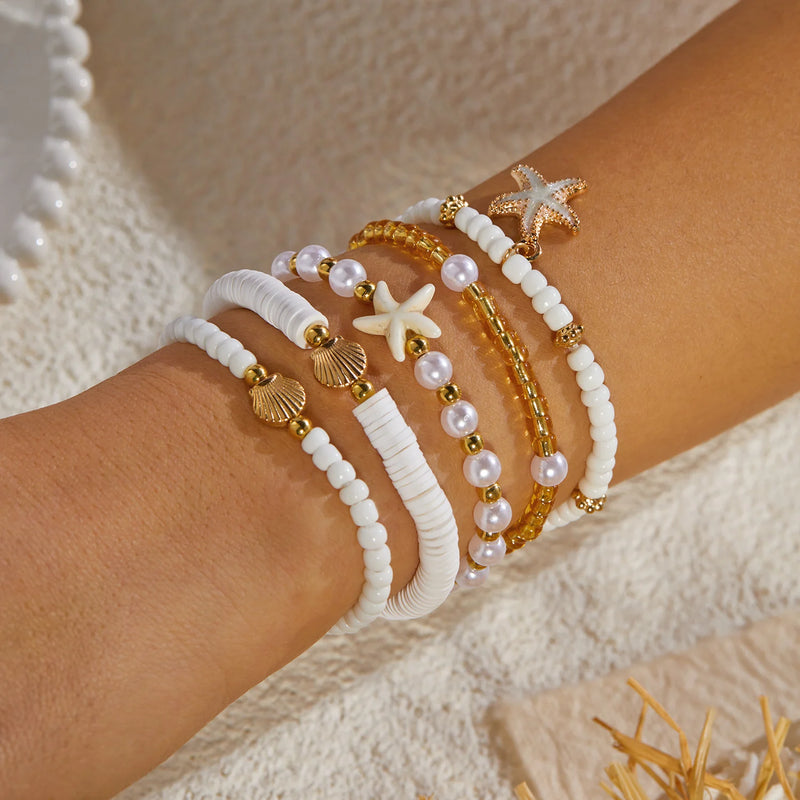 Gros plan sur un lot de 5 bracelets bohèmes avec perles heishi, coquillages et étoiles de mer sur un poignet