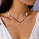Collier ras-du-cou coquillages cauris blancs et perles dorées porté par une femme