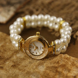 Montre bracelet à double rang de perles, cadran blanc et doré, posée sur tissu texturé