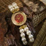 Montre chic à perles et cadran rouge, portée sur un support en bois avec plume dorée