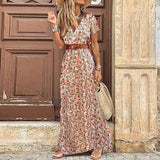 Femme portant une robe longue crème à motifs de petites fleurs rouges et orange, ceinture marron et chapeau de paille