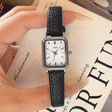 Montre femme vintage carrée GEDI, bracelet cuir noir, boîtier argenté, sur un livre ouvert