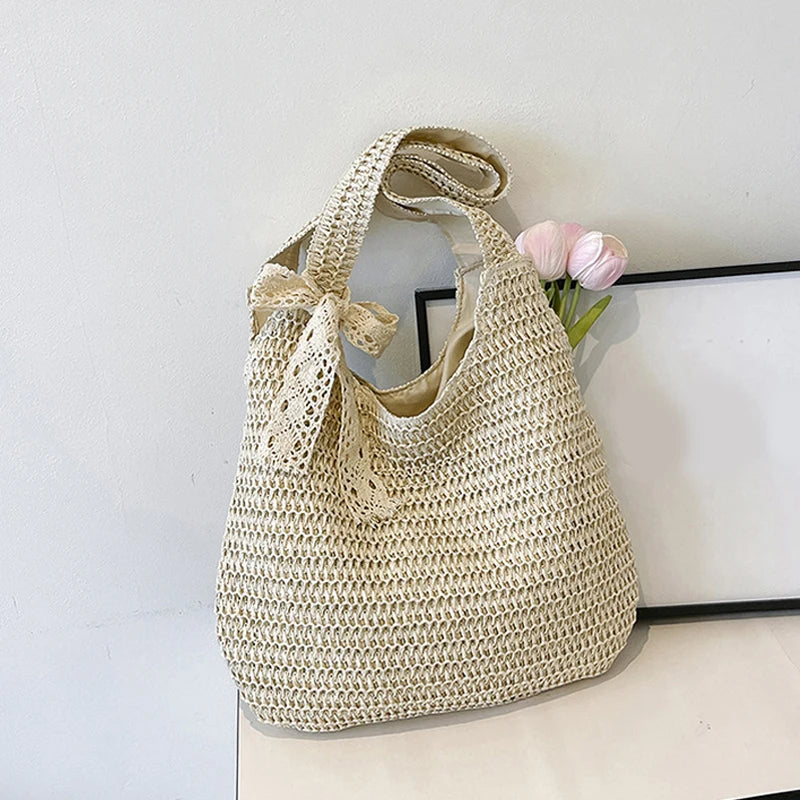 Sac de plage en paille tressée beige clair avec ruban en dentelle noué sur l'anse et fleur rose
