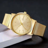 Montre dorée à cadran épuré et bracelet milanais sur fond sombre