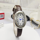 Montre ovale vintage avec bracelet en cuir marron et cadran argenté, posée sur un support