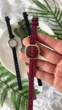 Montre carrée vintage pour femme avec bracelet en cuir bordeaux et cadran doré, tenue par une main