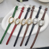 Montre ovale vintage avec bracelet en cuir noir, cadran doré, posée à plat