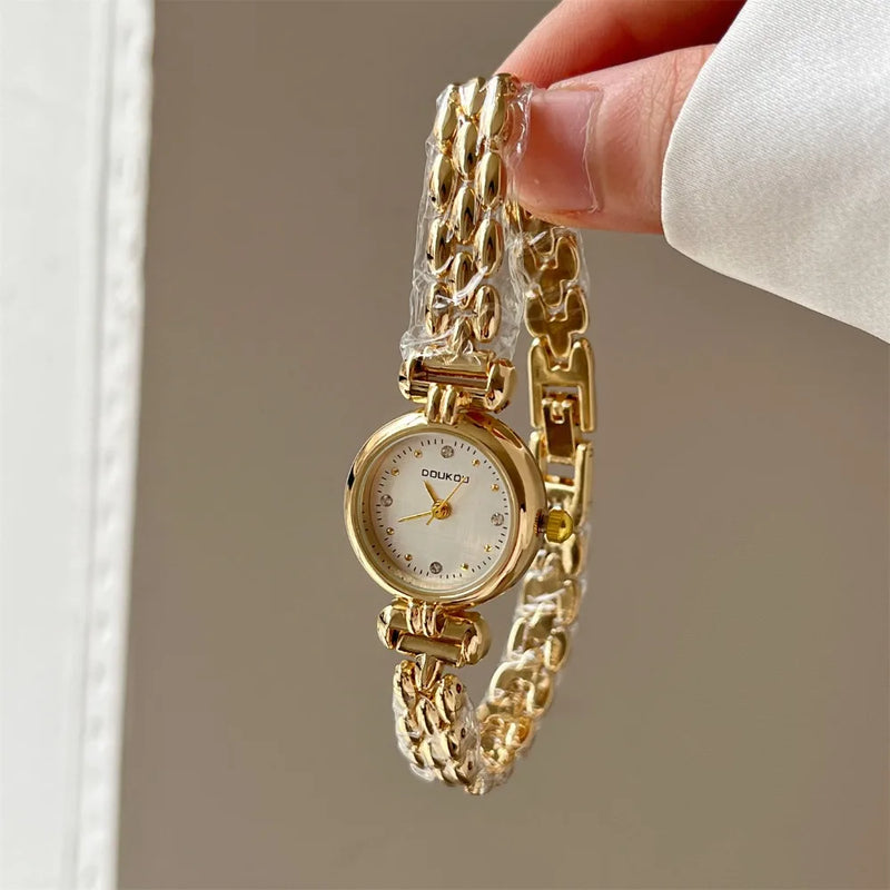 Montre bracelet femme dorée avec petit cadran blanc et strass, tenue à la main