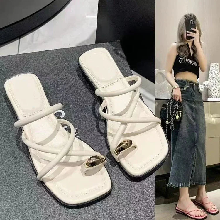 Paire de sandales plates blanches pour femme avec lanières croisées et détail doré, portées avec une jupe en jean