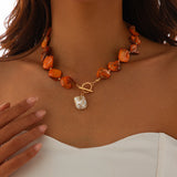 Collier bohème avec perles carrées oranges et pendentif perle baroque sur un décolleté blanc