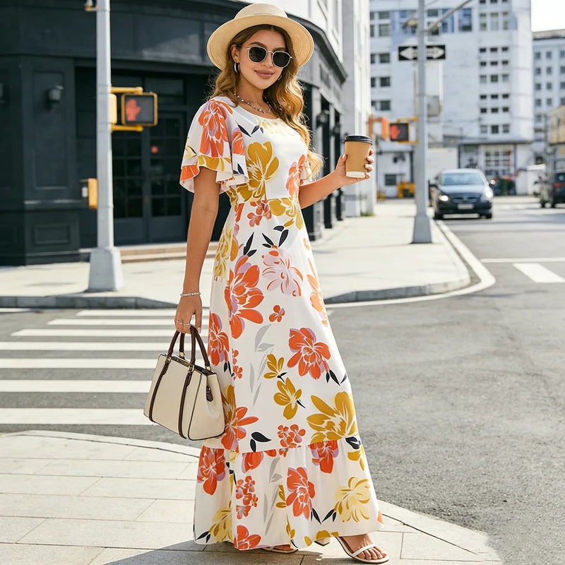 Femme élégante en robe longue fleurie orange et jaune, manches papillon, posant dans un environnement urbain