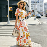 Femme élégante en robe longue fleurie orange et jaune, manches papillon, posant dans un environnement urbain