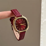 Gros plan sur une montre carrée vintage femme, bracelet en cuir bordeaux et cadran doré, tenue entre deux doigts