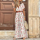 Femme portant une robe longue blanche à motifs de petites roses rouges et feuilles, ceinture marron et chapeau de paille